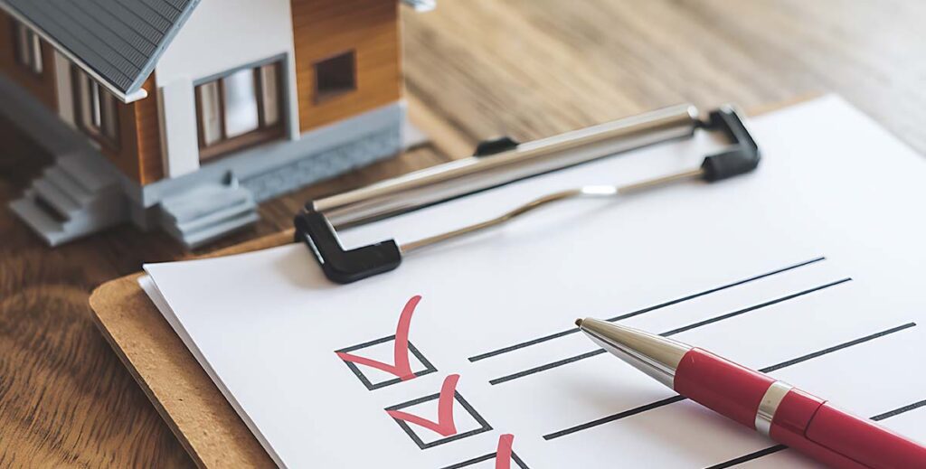 Furnace maintenance check list sitting on a desk with a pen next to it, and a miniature house to the left of the check list, on a table in Edmonton Alberta.